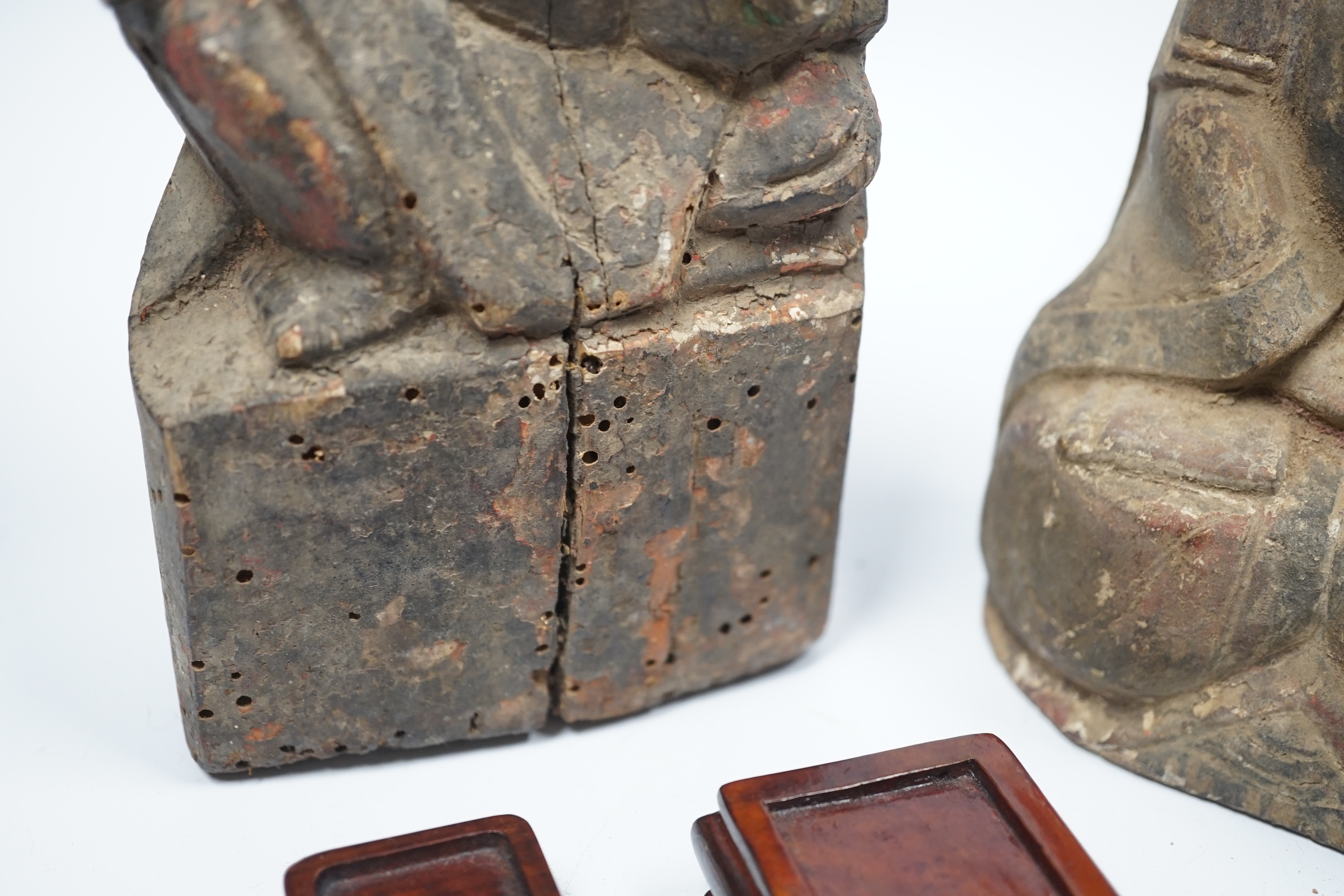 Two Chinese or Southeast Asian carved wood figures of seated immortals, and seven small wood stands, largest 24cm high